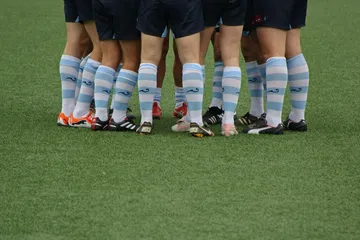 A rugby team’s legs in striped socks, gathered in a huddle on the pitch
